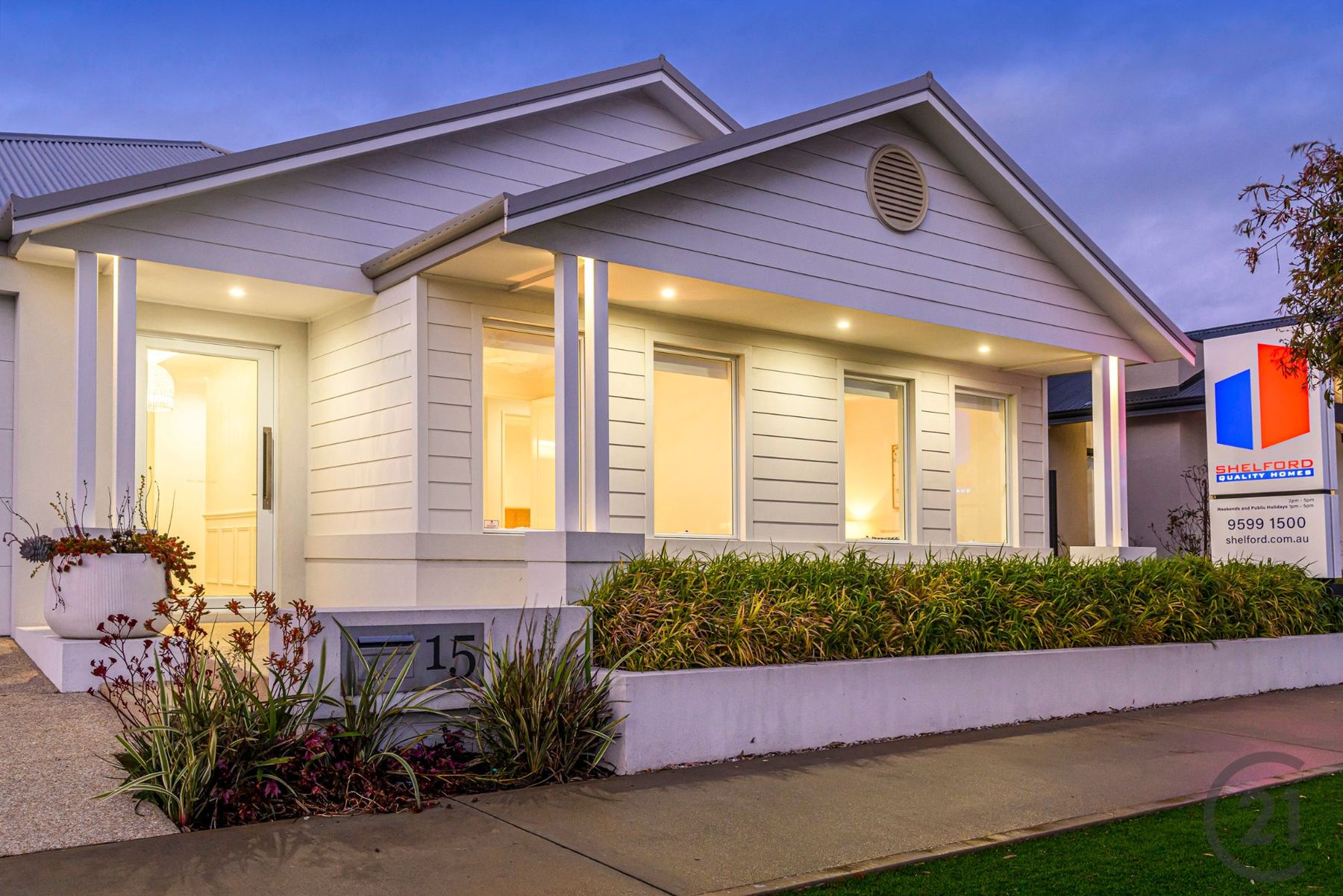 White weatherboard facade at dusk with lit porch columns and garden beds