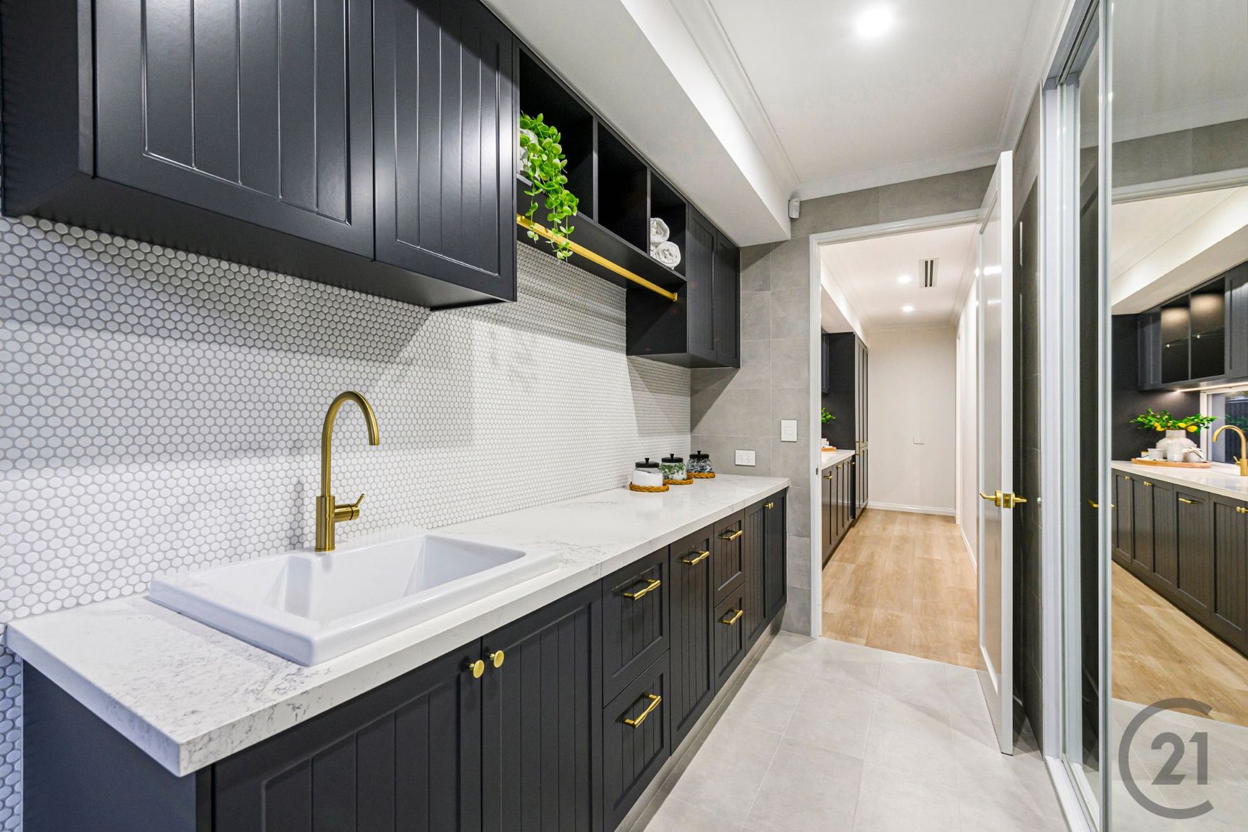 Laundry with charcoal cabinetry, penny-round tiles, brass hanging rail and mirrored storage