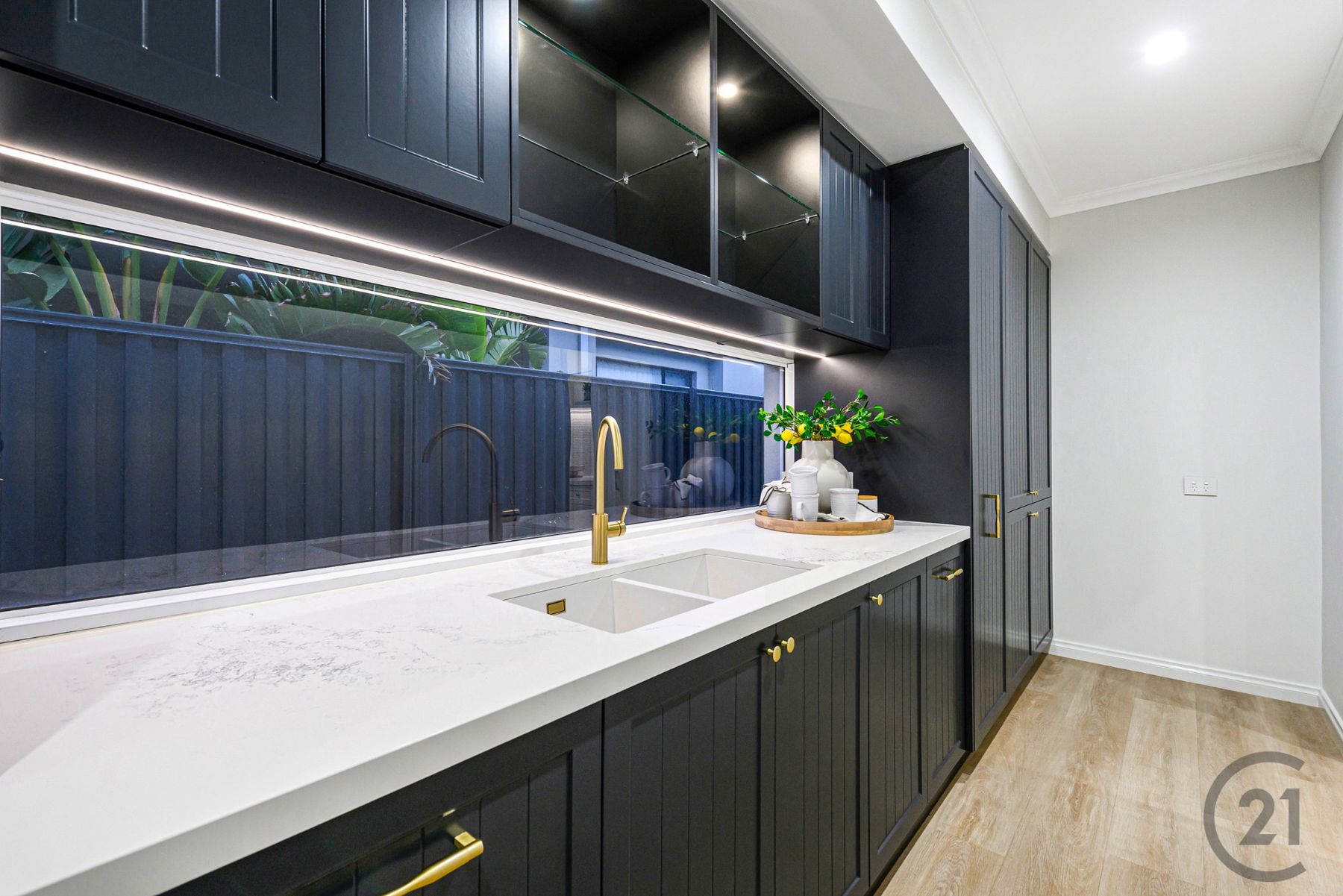 Scullery with charcoal cabinetry, double sink, brass tapware and a long window splashback